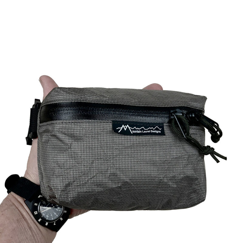 A man holds a MLD Pack Pocket in his hand. You can only see the tips of his thumb and forefinger.